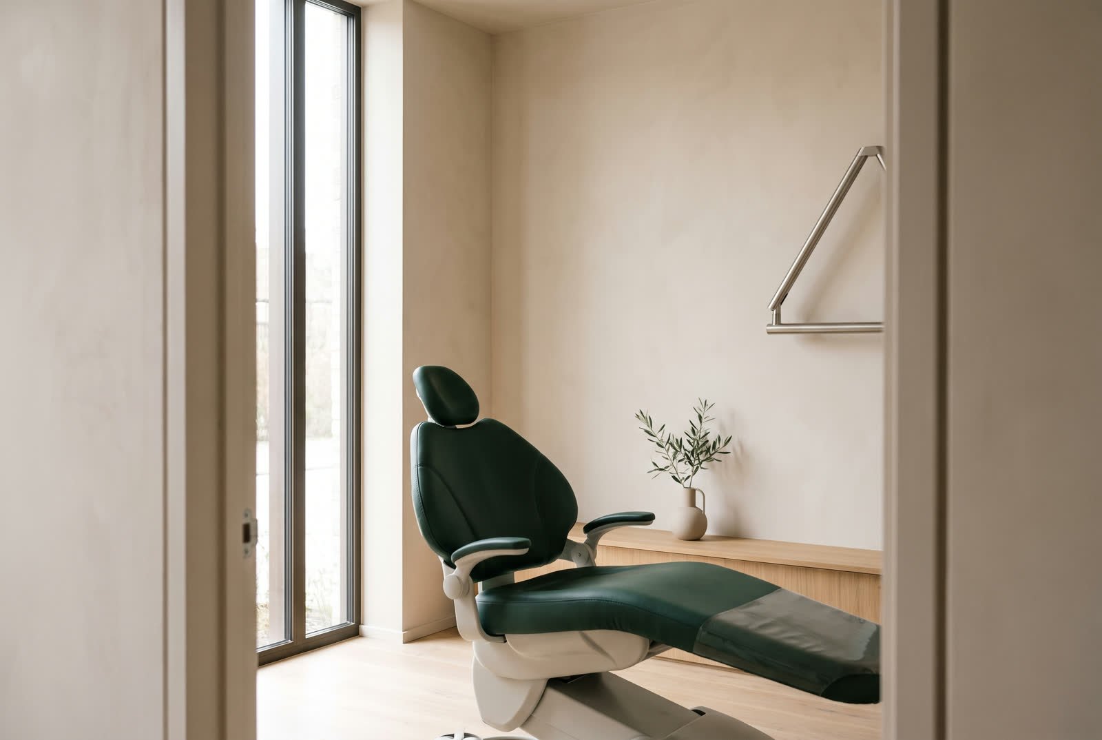 Sala de atendimento com parede clara, piso de madeira, cadeira verde e janela alta